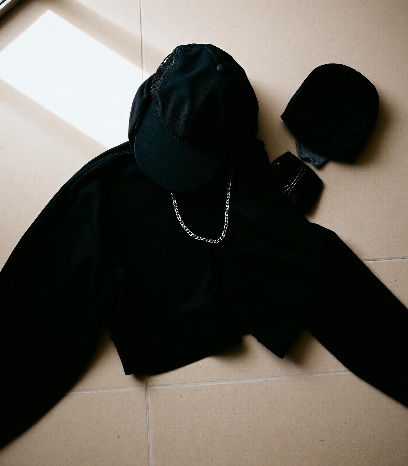 Composición flat lay de gorra negra, hoodie oversize y cadena plateada.